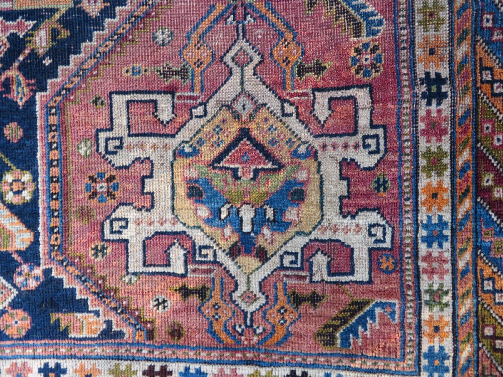 An antique Qashqai hand-knotted wool rug featuring a central diamond medallion surrounded by geometric tribal motifs in shades of navy blue, terracotta red, and cream. View XI