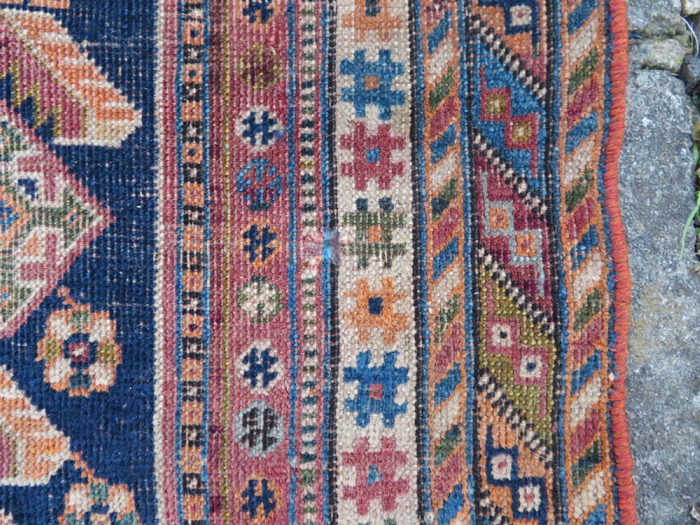 An antique Qashqai hand-knotted wool rug featuring a central diamond medallion surrounded by geometric tribal motifs in shades of navy blue, terracotta red, and cream. View XIII