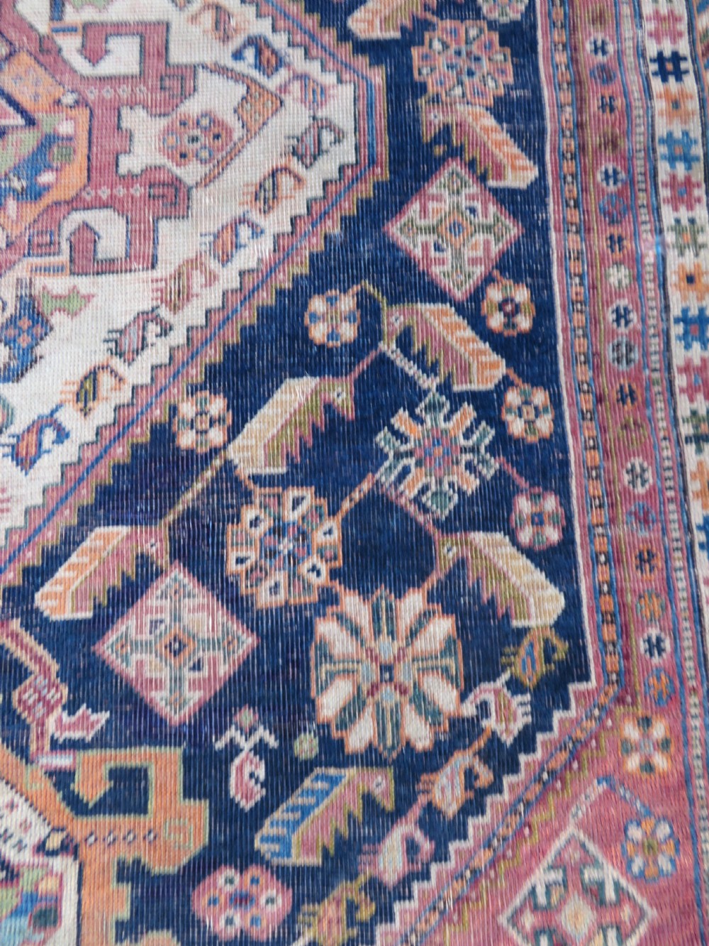 An antique Qashqai hand-knotted wool rug featuring a central diamond medallion surrounded by geometric tribal motifs in shades of navy blue, terracotta red, and cream. View XVII
