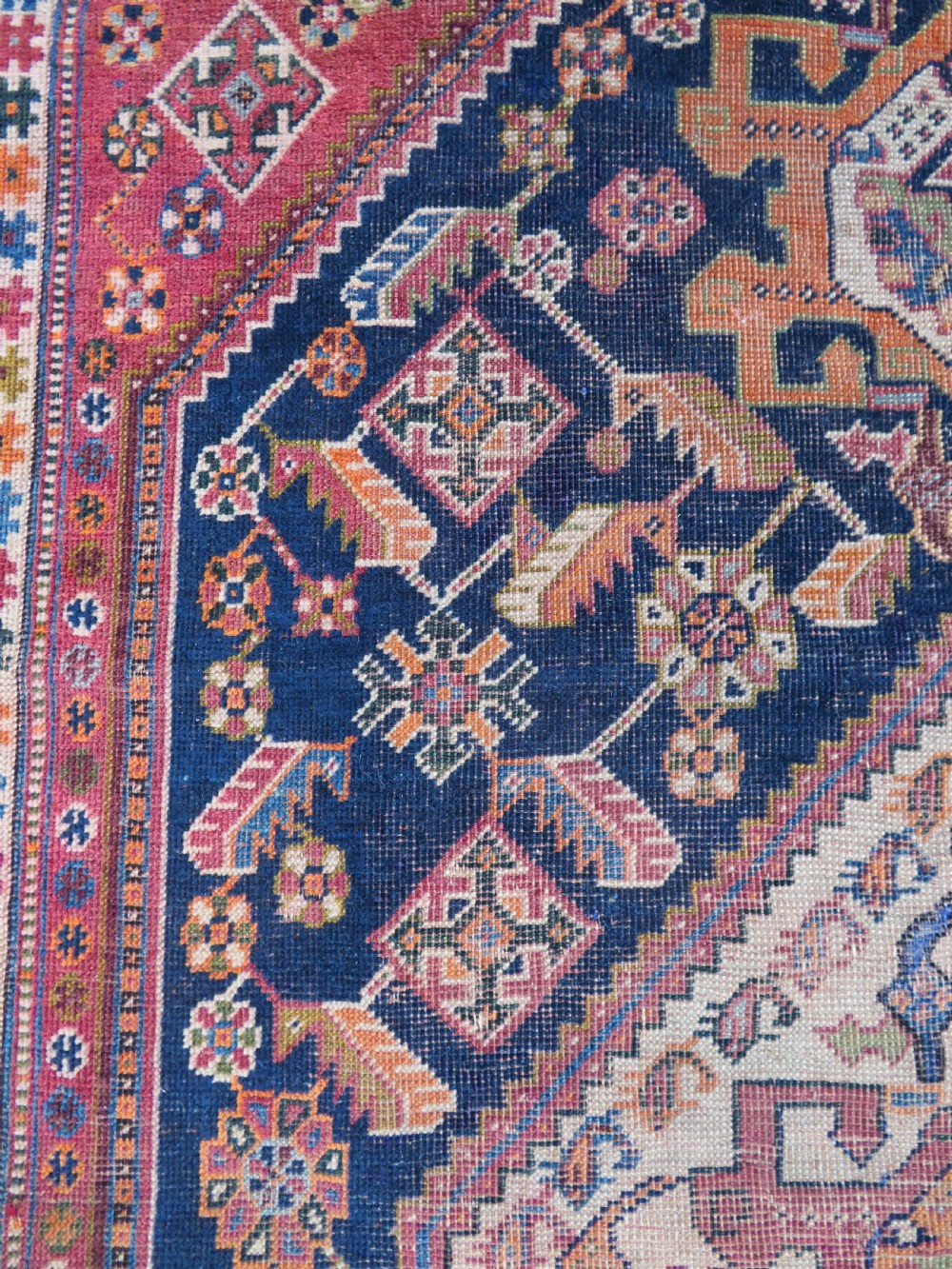 An antique Qashqai hand-knotted wool rug featuring a central diamond medallion surrounded by geometric tribal motifs in shades of navy blue, terracotta red, and cream. View XVIII