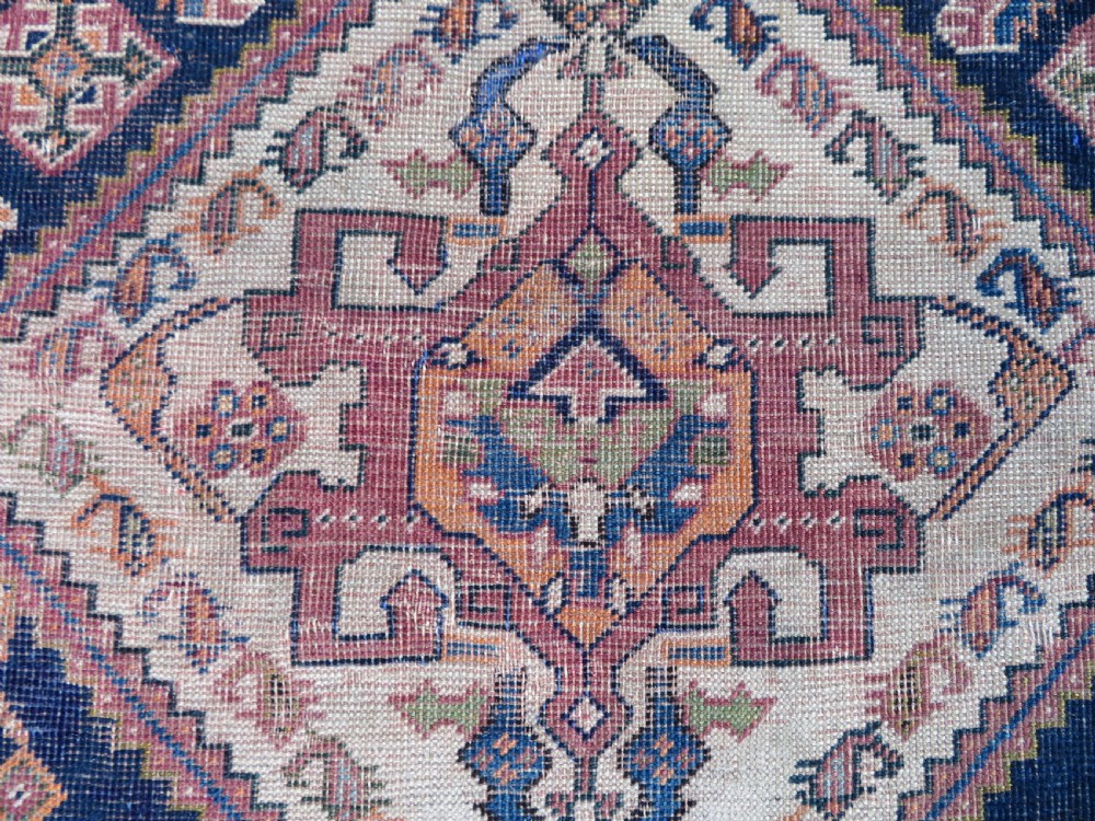 An antique Qashqai hand-knotted wool rug featuring a central diamond medallion surrounded by geometric tribal motifs in shades of navy blue, terracotta red, and cream. View XXII