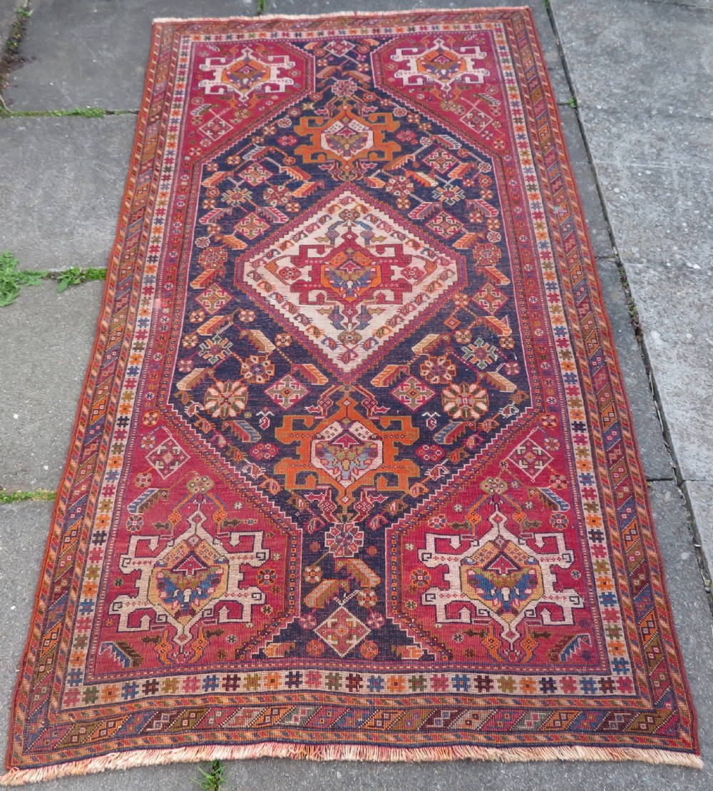 An antique Qashqai hand-knotted wool rug featuring a central diamond medallion surrounded by geometric tribal motifs in shades of navy blue, terracotta red, and cream. View XXIII
