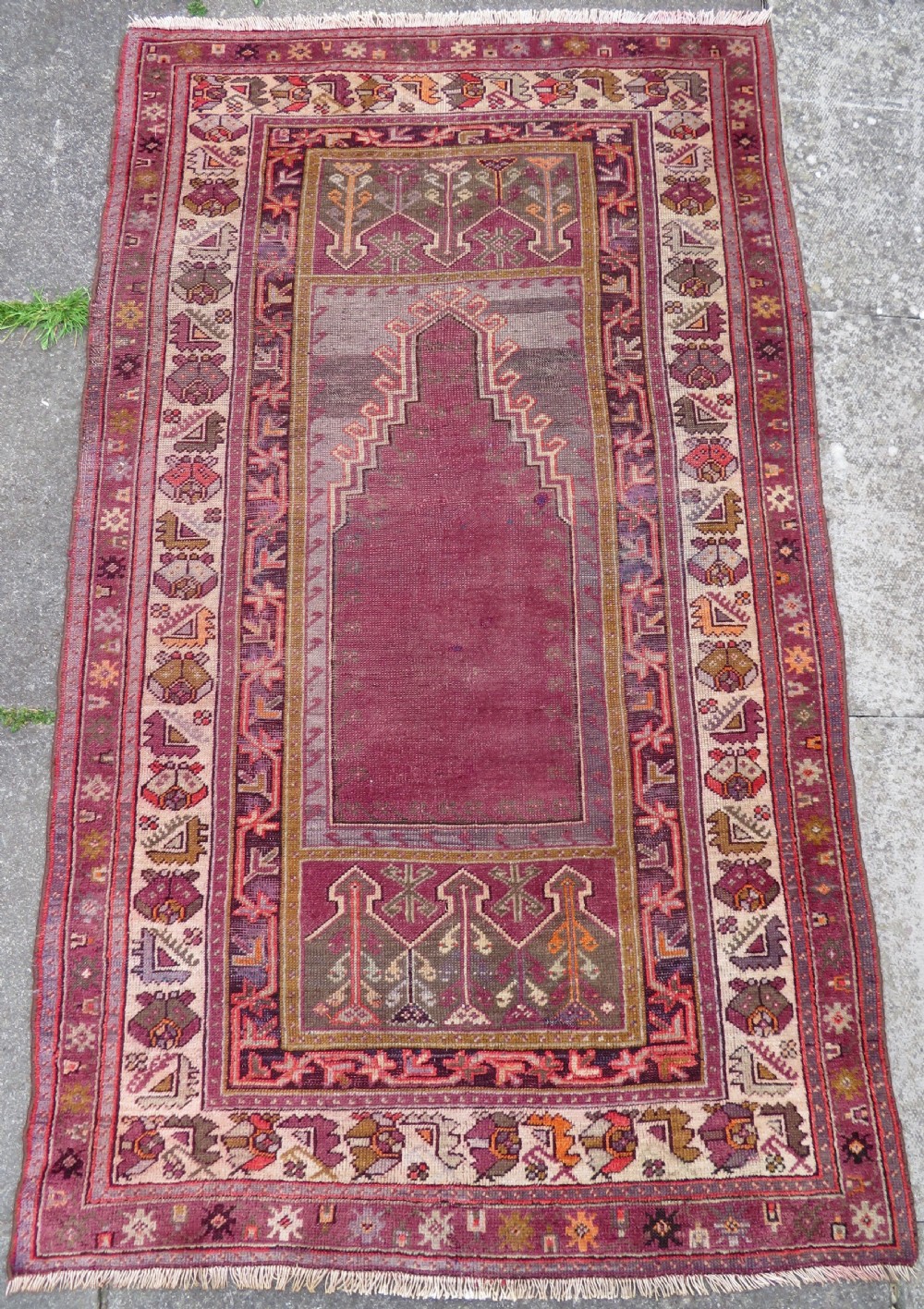 A late 19th-century hand-knotted Anatolian prayer rug featuring a deep magenta mihrab motif framed by geometric patterned borders in cream, ochre, and purple tones.
