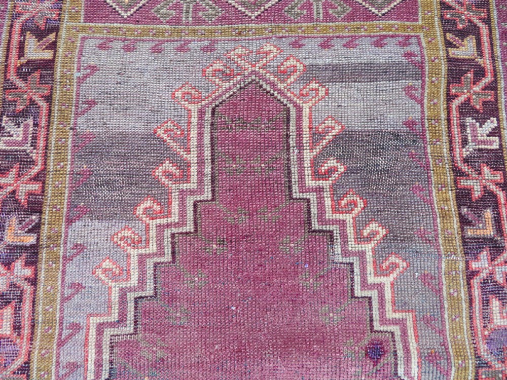 A late 19th-century hand-knotted Anatolian prayer rug featuring a deep magenta mihrab motif framed by geometric patterned borders in cream, ochre, and purple tones. View III