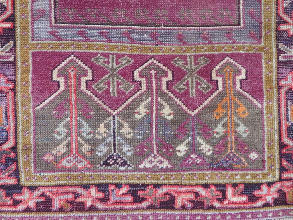 A late 19th-century hand-knotted Anatolian prayer rug featuring a deep magenta mihrab motif framed by geometric patterned borders in cream, ochre, and purple tones. View IV