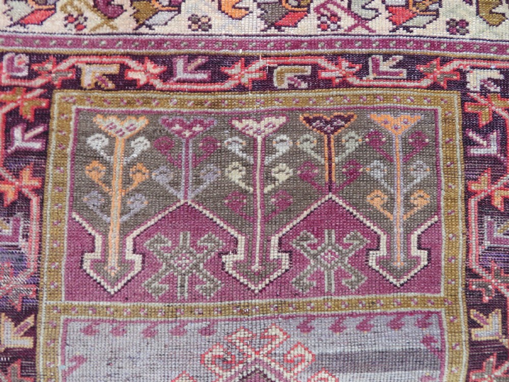 A late 19th-century hand-knotted Anatolian prayer rug featuring a deep magenta mihrab motif framed by geometric patterned borders in cream, ochre, and purple tones. View V