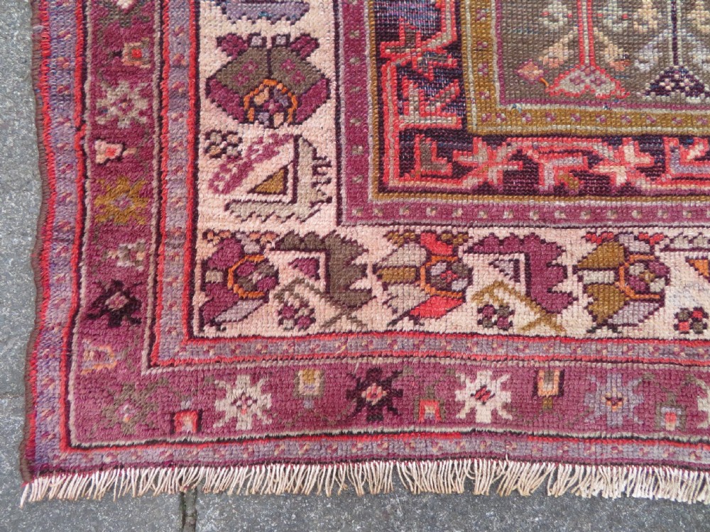 A late 19th-century hand-knotted Anatolian prayer rug featuring a deep magenta mihrab motif framed by geometric patterned borders in cream, ochre, and purple tones. View IX