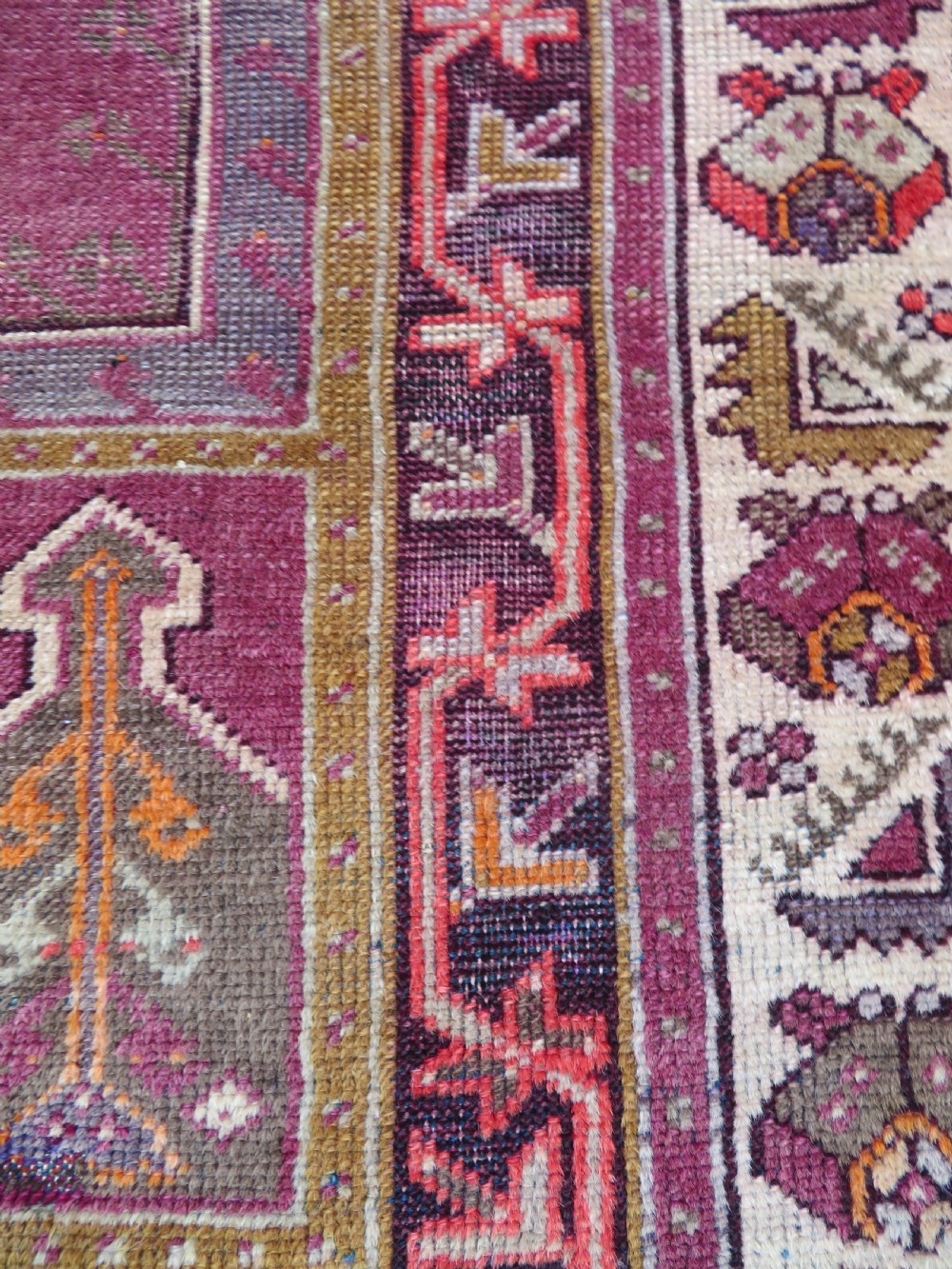 A late 19th-century hand-knotted Anatolian prayer rug featuring a deep magenta mihrab motif framed by geometric patterned borders in cream, ochre, and purple tones. View X