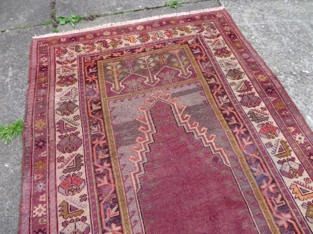 A late 19th-century hand-knotted Anatolian prayer rug featuring a deep magenta mihrab motif framed by geometric patterned borders in cream, ochre, and purple tones. View XI