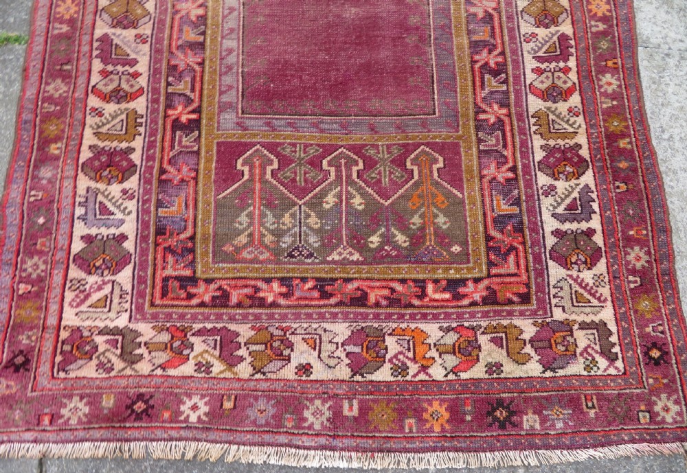 A late 19th-century hand-knotted Anatolian prayer rug featuring a deep magenta mihrab motif framed by geometric patterned borders in cream, ochre, and purple tones. View XII