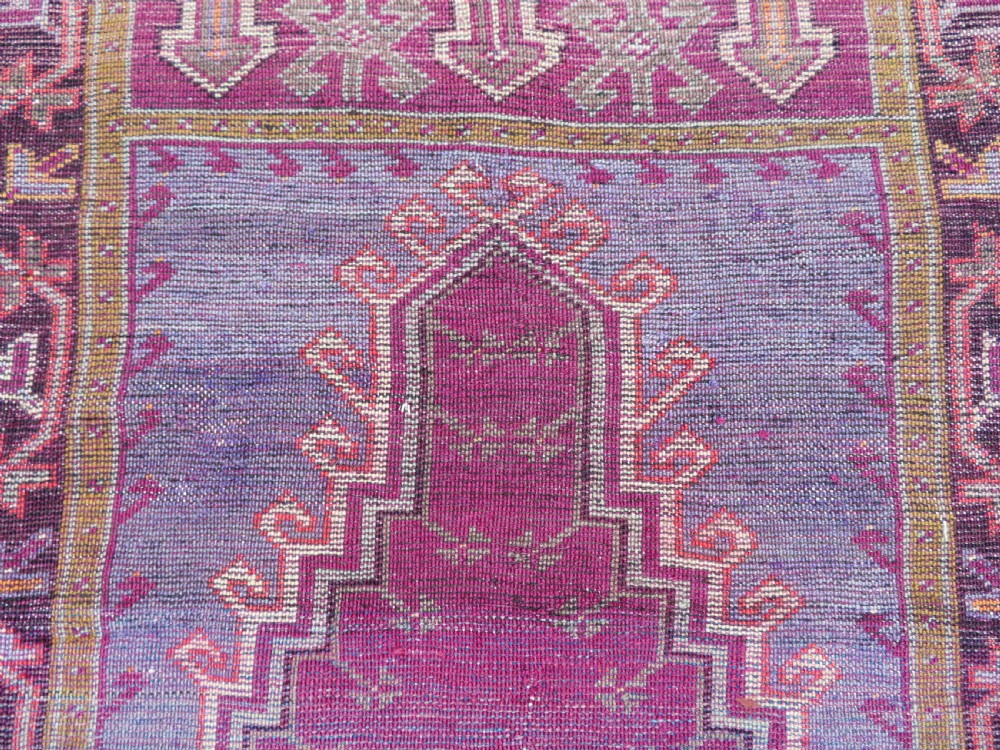 A late 19th-century hand-knotted Anatolian prayer rug featuring a deep magenta mihrab motif framed by geometric patterned borders in cream, ochre, and purple tones. View XVII