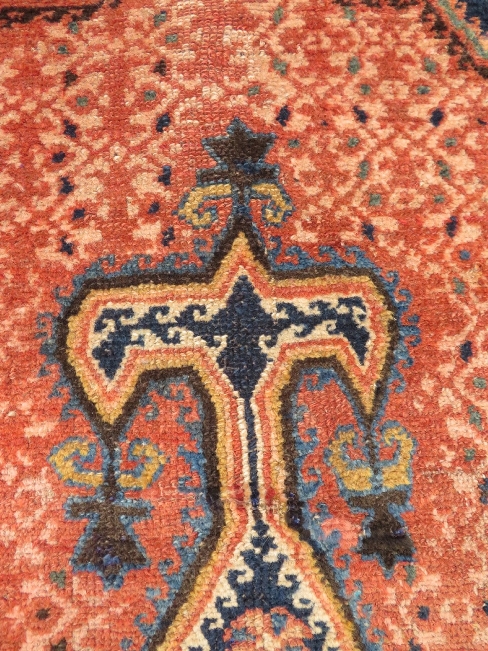 A long, narrow hand-knotted Kurdish runner rug featuring diamond medallions in navy and terracotta on a patterned rust-red field with decorative borders. View IX