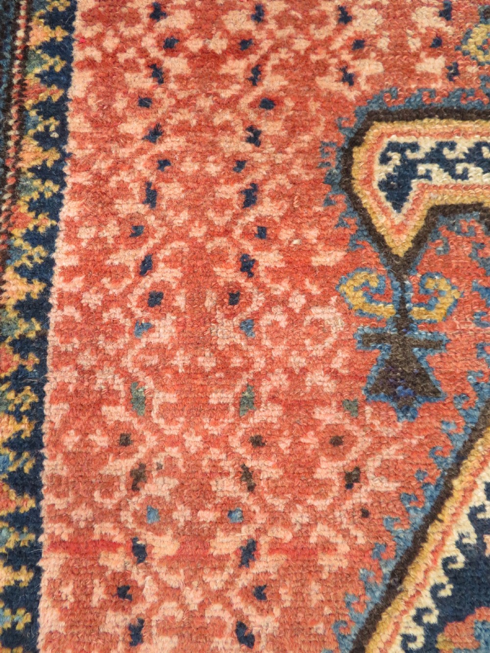 A long, narrow hand-knotted Kurdish runner rug featuring diamond medallions in navy and terracotta on a patterned rust-red field with decorative borders. View X