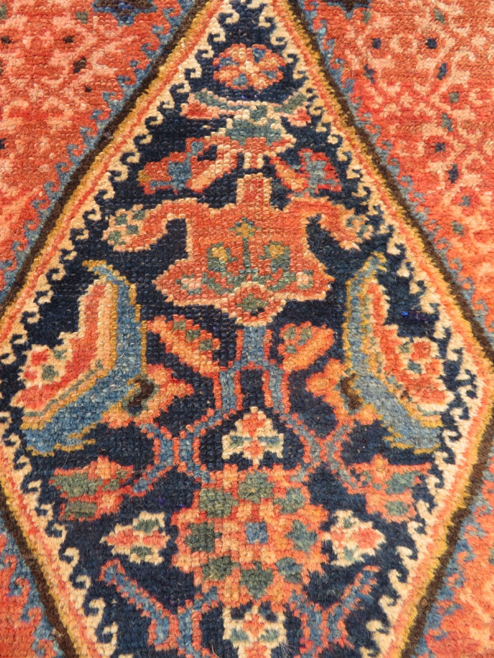 A long, narrow hand-knotted Kurdish runner rug featuring diamond medallions in navy and terracotta on a patterned rust-red field with decorative borders. View XI