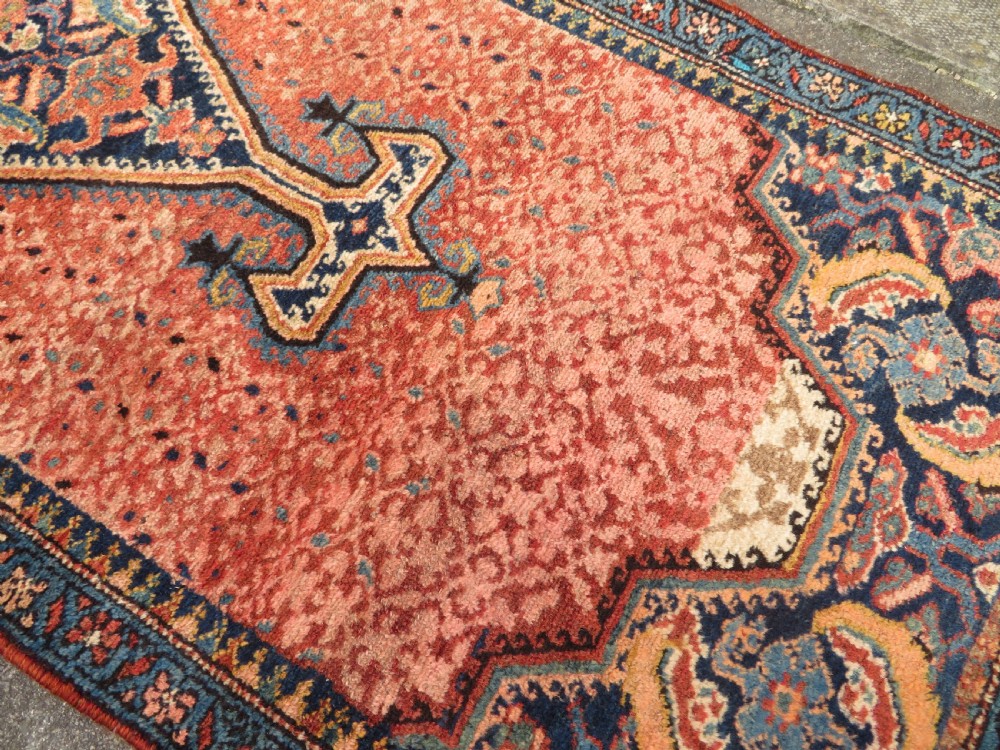 A long, narrow hand-knotted Kurdish runner rug featuring diamond medallions in navy and terracotta on a patterned rust-red field with decorative borders. View XIII