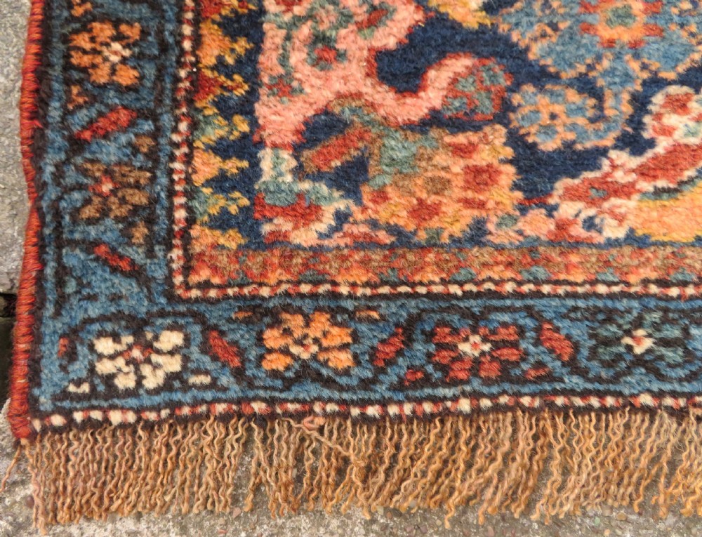 A long, narrow hand-knotted Kurdish runner rug featuring diamond medallions in navy and terracotta on a patterned rust-red field with decorative borders. View XIV