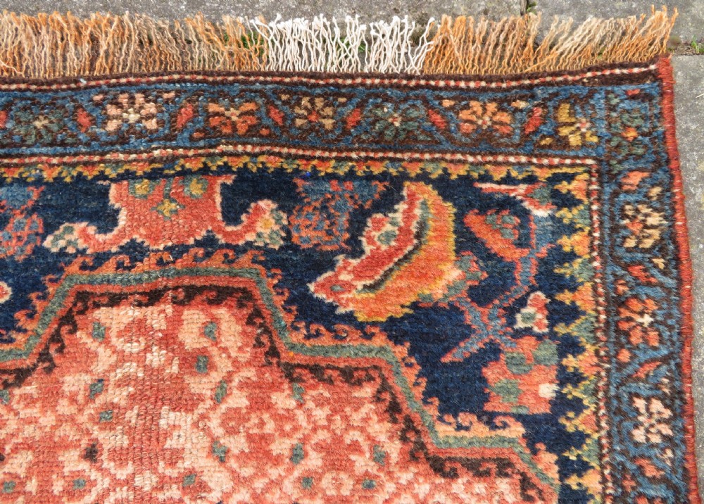 A long, narrow hand-knotted Kurdish runner rug featuring diamond medallions in navy and terracotta on a patterned rust-red field with decorative borders. View XVII