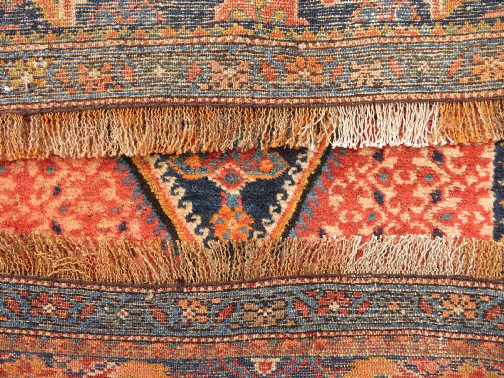 A long, narrow hand-knotted Kurdish runner rug featuring diamond medallions in navy and terracotta on a patterned rust-red field with decorative borders. View XXI