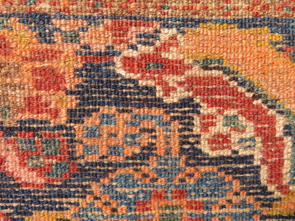 A long, narrow hand-knotted Kurdish runner rug featuring diamond medallions in navy and terracotta on a patterned rust-red field with decorative borders. View XXIII