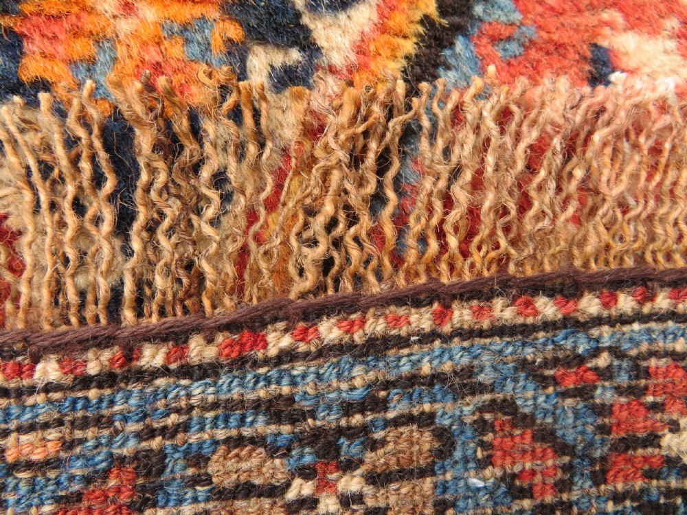 A long, narrow hand-knotted Kurdish runner rug featuring diamond medallions in navy and terracotta on a patterned rust-red field with decorative borders. View XXIV