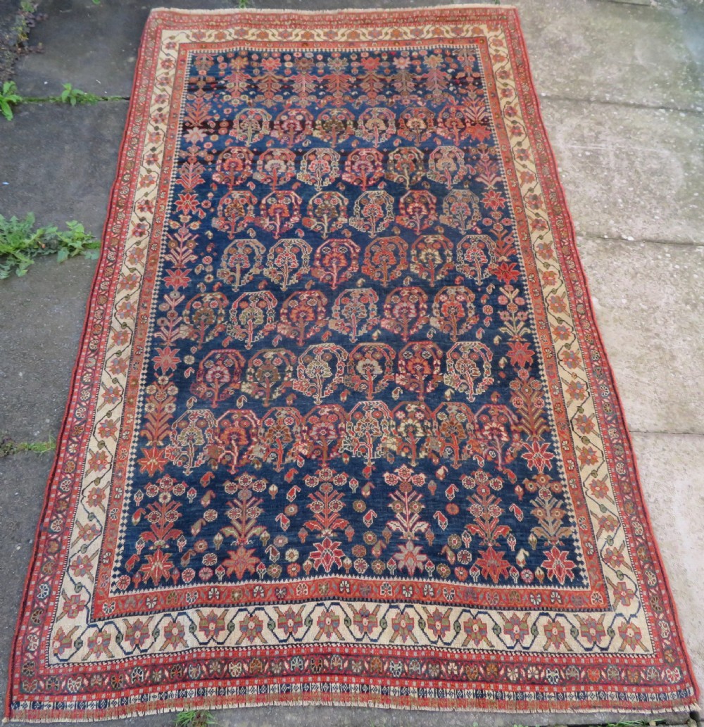 An antique Persian Qashqai Kashkuli wool rug featuring repeating boteh patterns on a deep indigo blue field surrounded by intricate cream and terracotta floral borders.