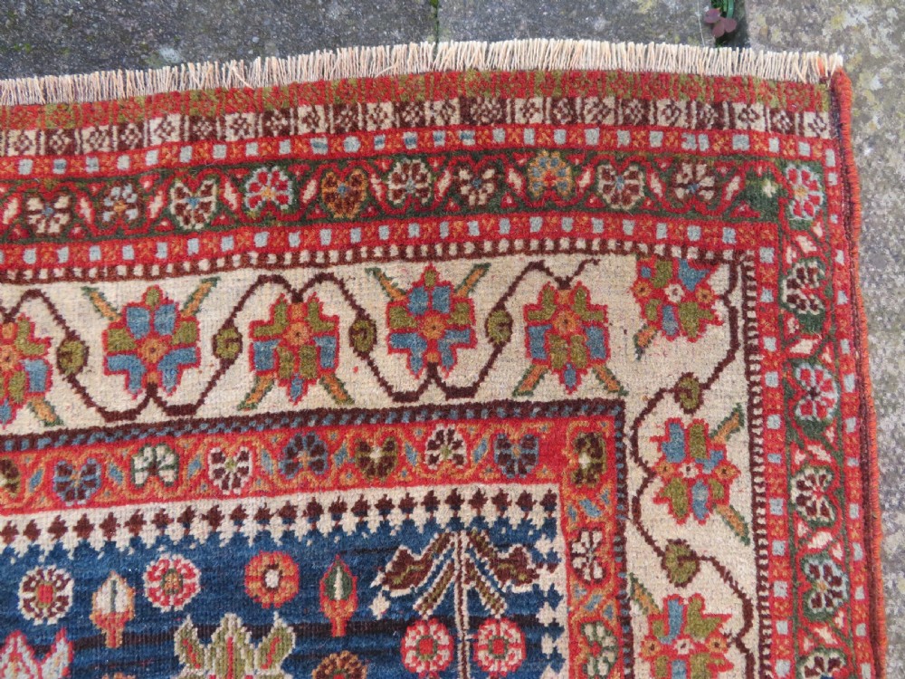 An antique Persian Qashqai Kashkuli wool rug featuring repeating boteh patterns on a deep indigo blue field surrounded by intricate cream and terracotta floral borders. View X