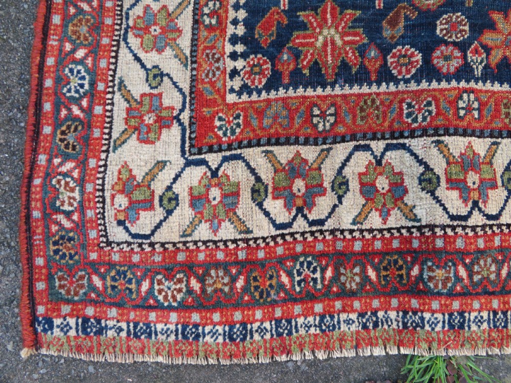 An antique Persian Qashqai Kashkuli wool rug featuring repeating boteh patterns on a deep indigo blue field surrounded by intricate cream and terracotta floral borders. View XI