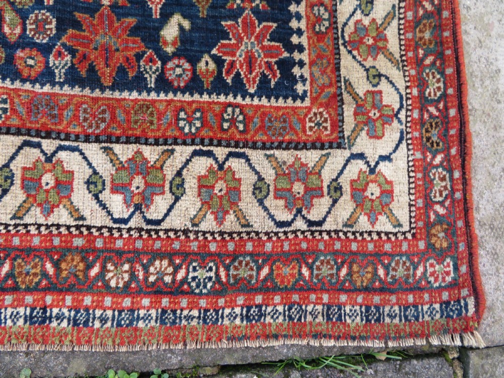 An antique Persian Qashqai Kashkuli wool rug featuring repeating boteh patterns on a deep indigo blue field surrounded by intricate cream and terracotta floral borders. View XII