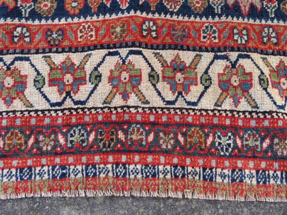 An antique Persian Qashqai Kashkuli wool rug featuring repeating boteh patterns on a deep indigo blue field surrounded by intricate cream and terracotta floral borders. View XIII