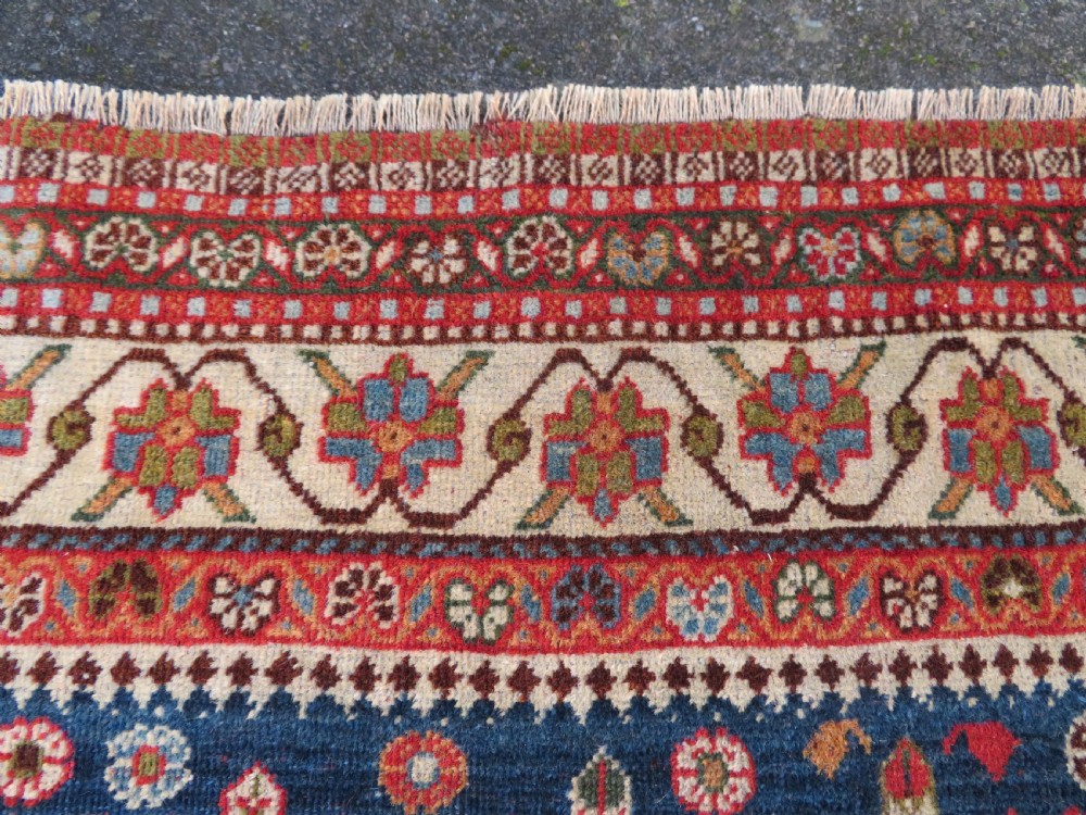 An antique Persian Qashqai Kashkuli wool rug featuring repeating boteh patterns on a deep indigo blue field surrounded by intricate cream and terracotta floral borders. View XIX