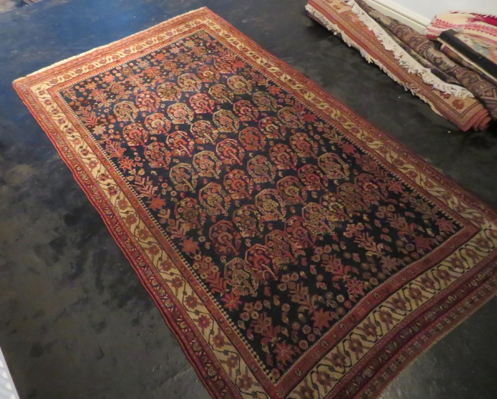An antique Persian Qashqai Kashkuli wool rug featuring repeating boteh patterns on a deep indigo blue field surrounded by intricate cream and terracotta floral borders. View XXVII