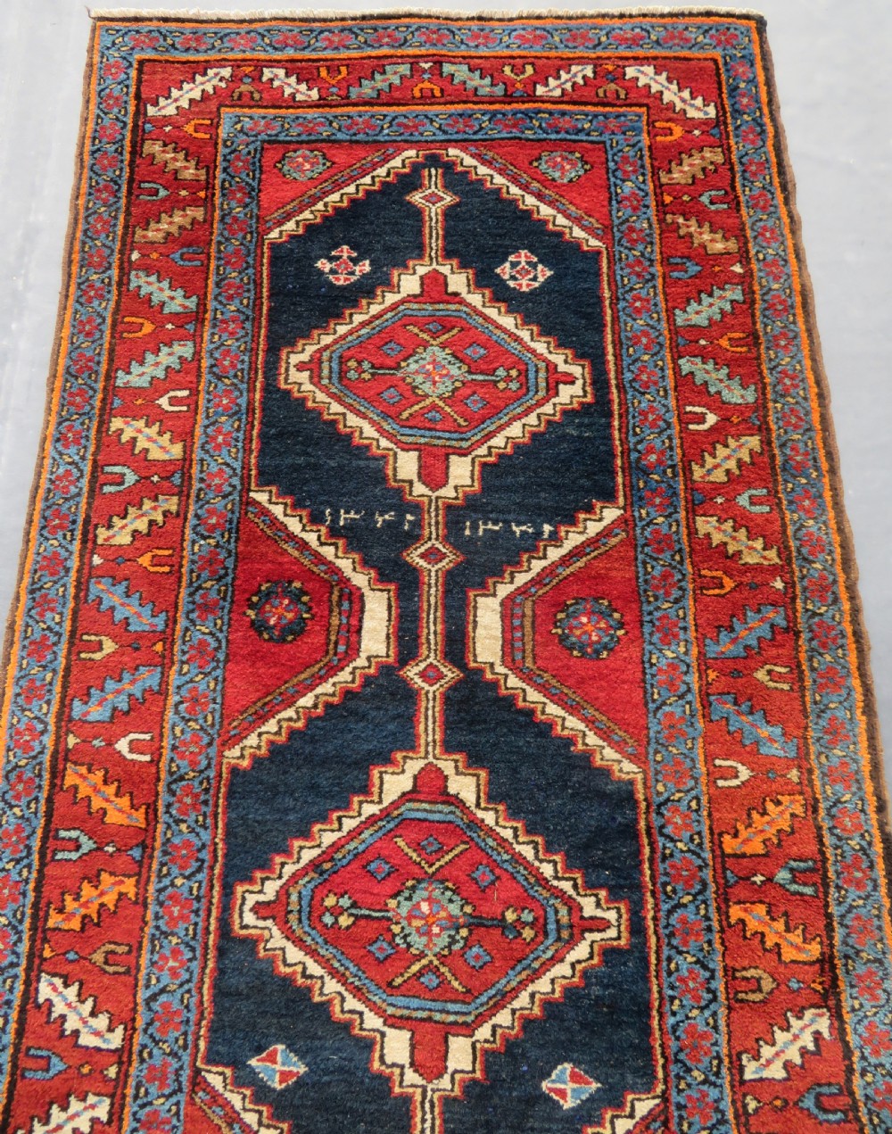 A long antique Persian Kelardasht runner rug featuring geometric diamond medallions on a dark navy blue central field framed by red and blue patterned borders. View III