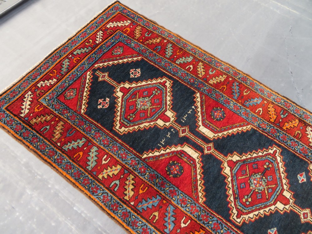 A long antique Persian Kelardasht runner rug featuring geometric diamond medallions on a dark navy blue central field framed by red and blue patterned borders. View XII
