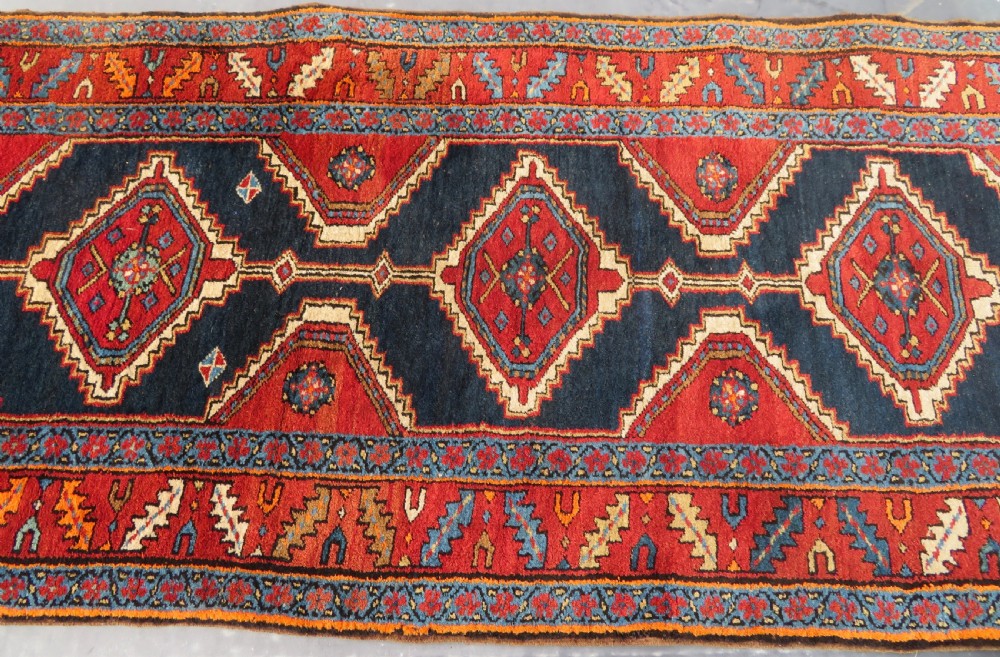 A long antique Persian Kelardasht runner rug featuring geometric diamond medallions on a dark navy blue central field framed by red and blue patterned borders. View XIV