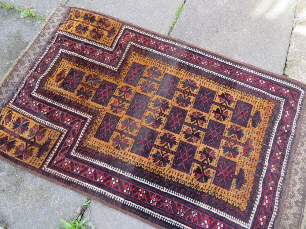 An antique Baluch wool prayer rug featuring a stepped arched mihrab design on a camel-coloured field with deep red and navy geometric motifs. View II