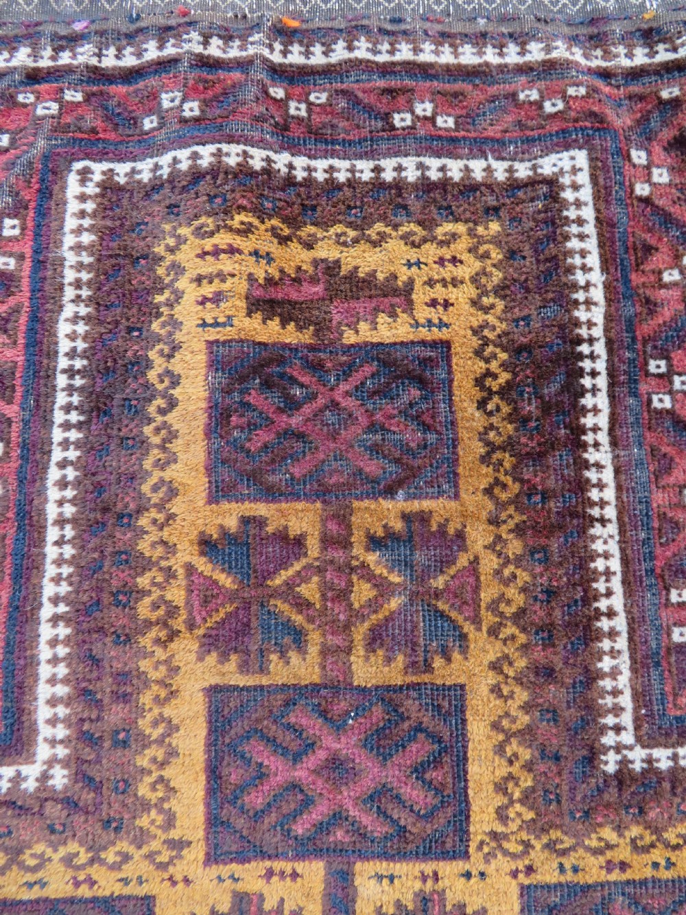 An antique Baluch wool prayer rug featuring a stepped arched mihrab design on a camel-coloured field with deep red and navy geometric motifs. View III