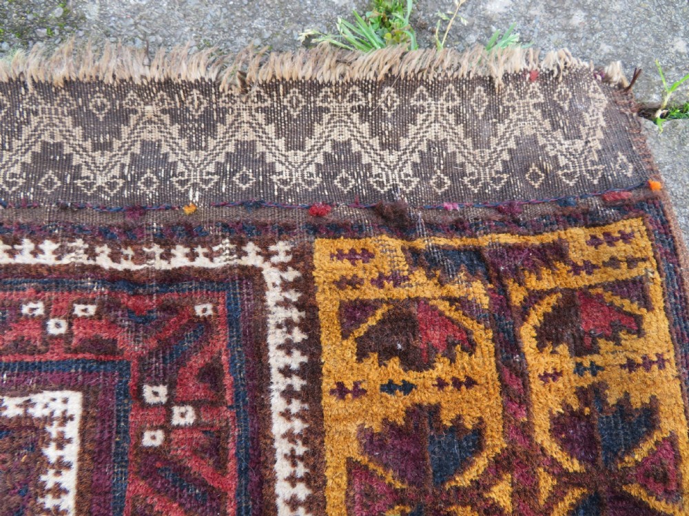 An antique Baluch wool prayer rug featuring a stepped arched mihrab design on a camel-coloured field with deep red and navy geometric motifs. View IV
