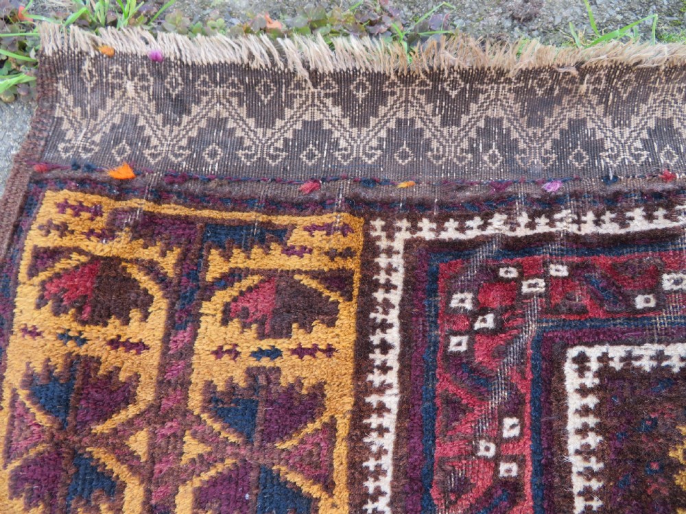 An antique Baluch wool prayer rug featuring a stepped arched mihrab design on a camel-coloured field with deep red and navy geometric motifs. View V