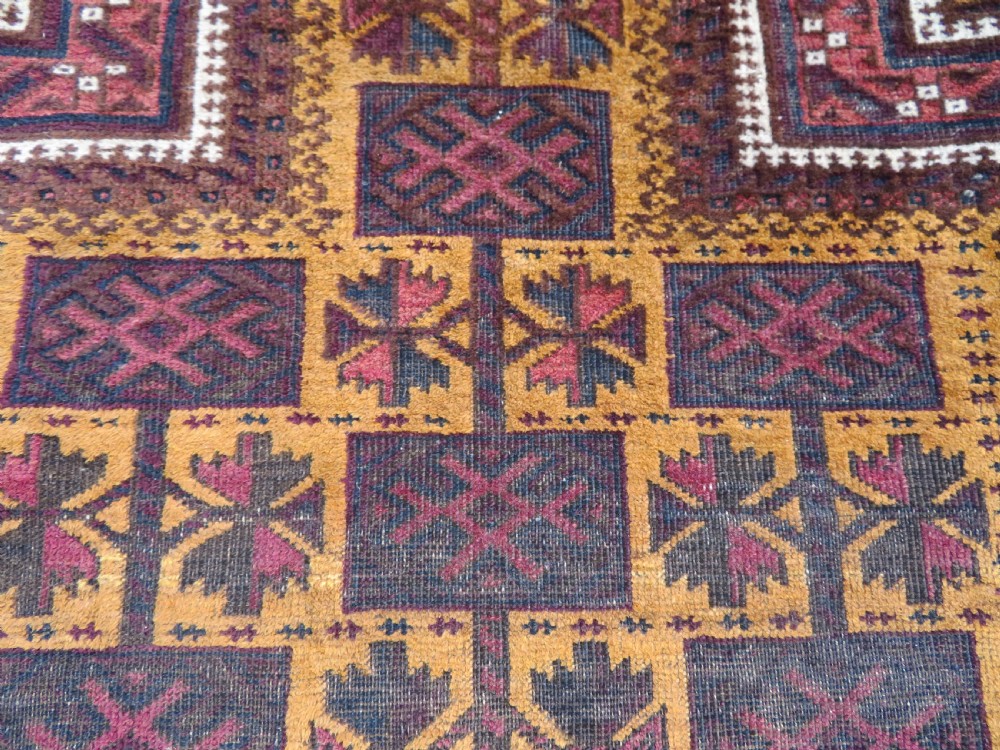 An antique Baluch wool prayer rug featuring a stepped arched mihrab design on a camel-coloured field with deep red and navy geometric motifs. View VI