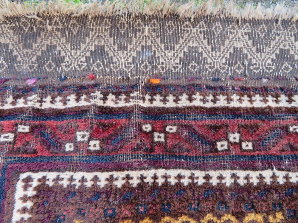 An antique Baluch wool prayer rug featuring a stepped arched mihrab design on a camel-coloured field with deep red and navy geometric motifs. View VII