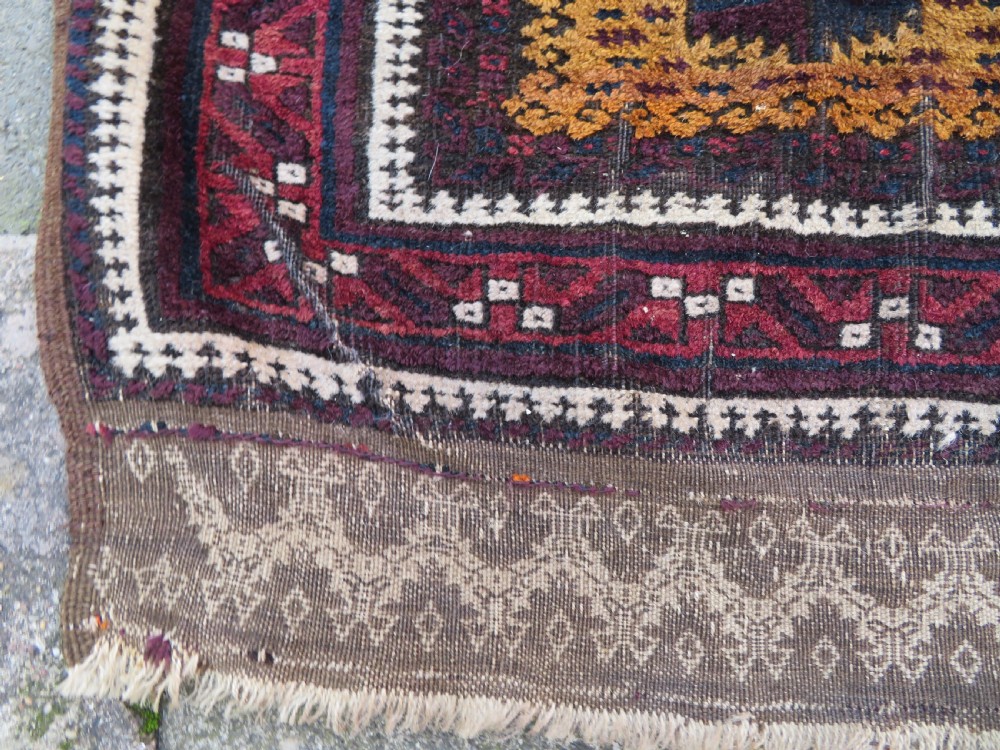 An antique Baluch wool prayer rug featuring a stepped arched mihrab design on a camel-coloured field with deep red and navy geometric motifs. View VIII