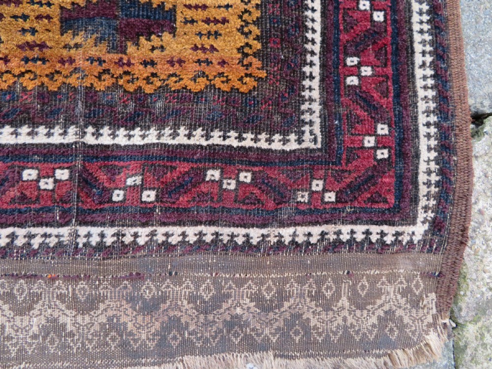 An antique Baluch wool prayer rug featuring a stepped arched mihrab design on a camel-coloured field with deep red and navy geometric motifs. View IX