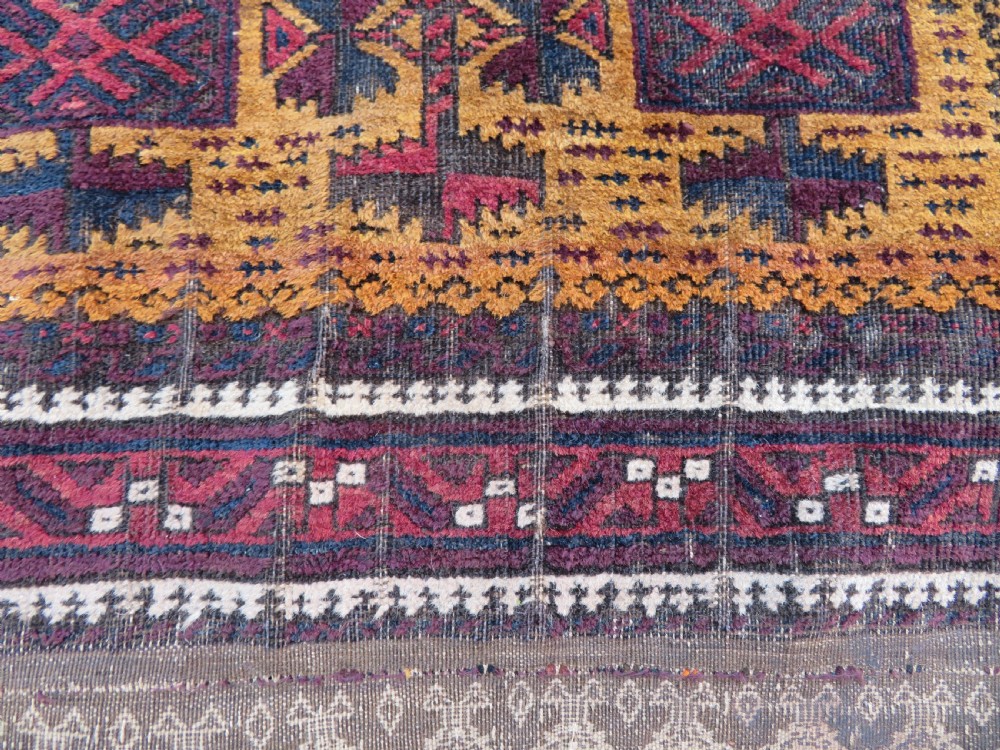 An antique Baluch wool prayer rug featuring a stepped arched mihrab design on a camel-coloured field with deep red and navy geometric motifs. View X