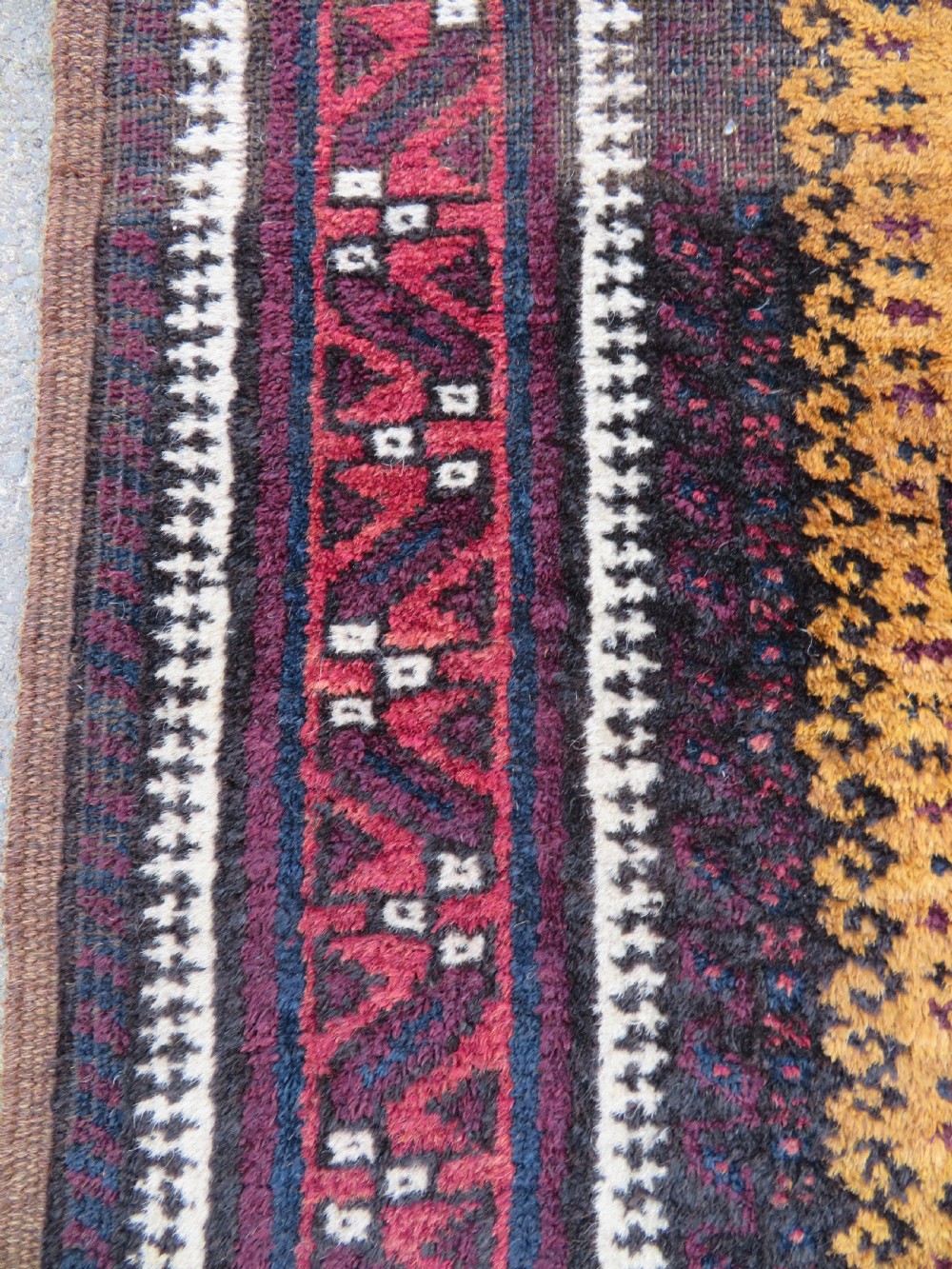 An antique Baluch wool prayer rug featuring a stepped arched mihrab design on a camel-coloured field with deep red and navy geometric motifs. View XI