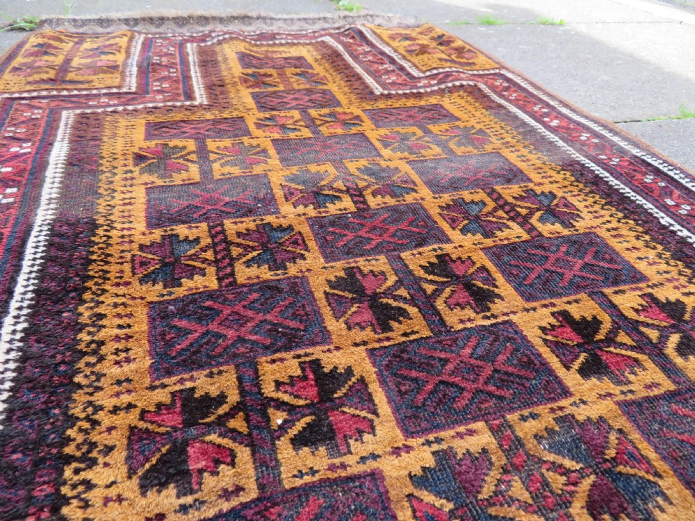 An antique Baluch wool prayer rug featuring a stepped arched mihrab design on a camel-coloured field with deep red and navy geometric motifs. View XII