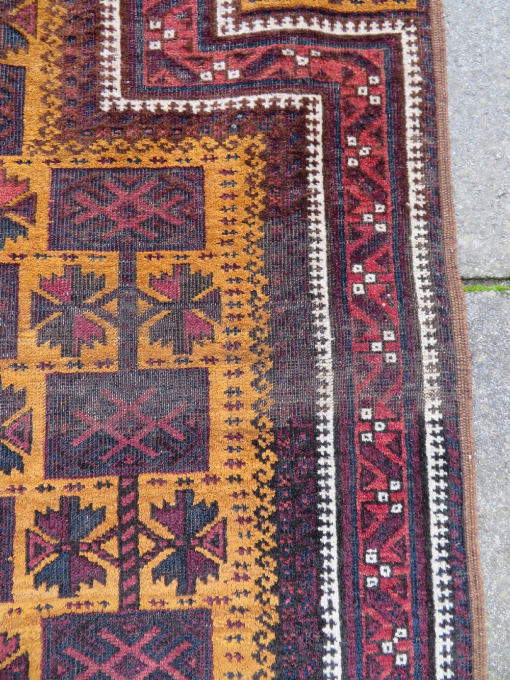An antique Baluch wool prayer rug featuring a stepped arched mihrab design on a camel-coloured field with deep red and navy geometric motifs. View XIII