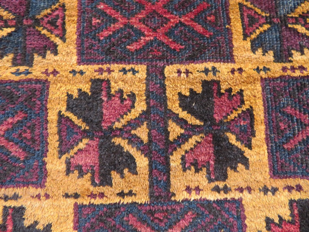 An antique Baluch wool prayer rug featuring a stepped arched mihrab design on a camel-coloured field with deep red and navy geometric motifs. View XIV
