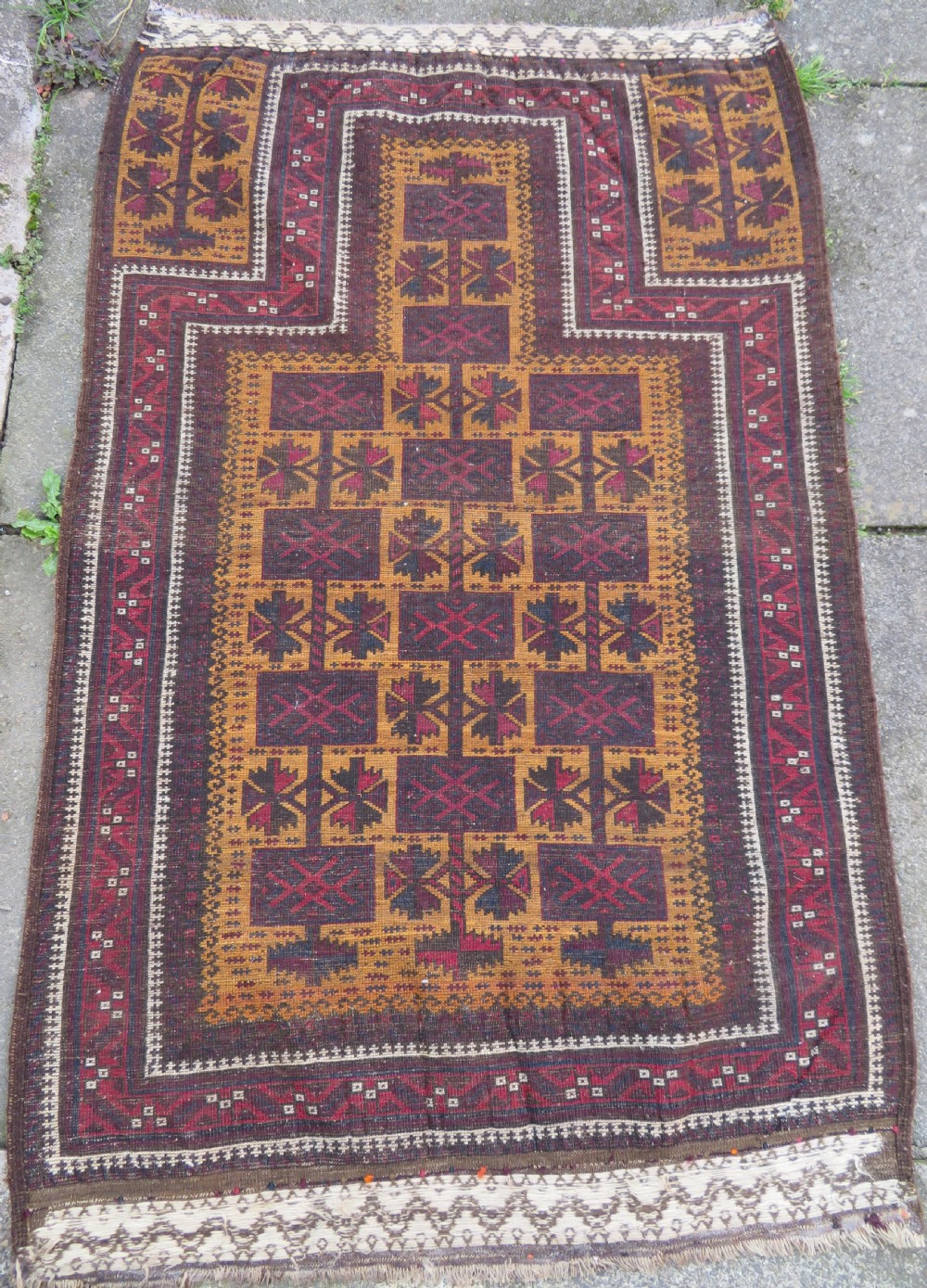 An antique Baluch wool prayer rug featuring a stepped arched mihrab design on a camel-coloured field with deep red and navy geometric motifs. View XVI