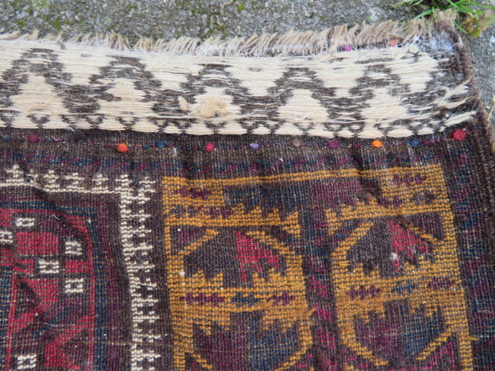 An antique Baluch wool prayer rug featuring a stepped arched mihrab design on a camel-coloured field with deep red and navy geometric motifs. View XVII