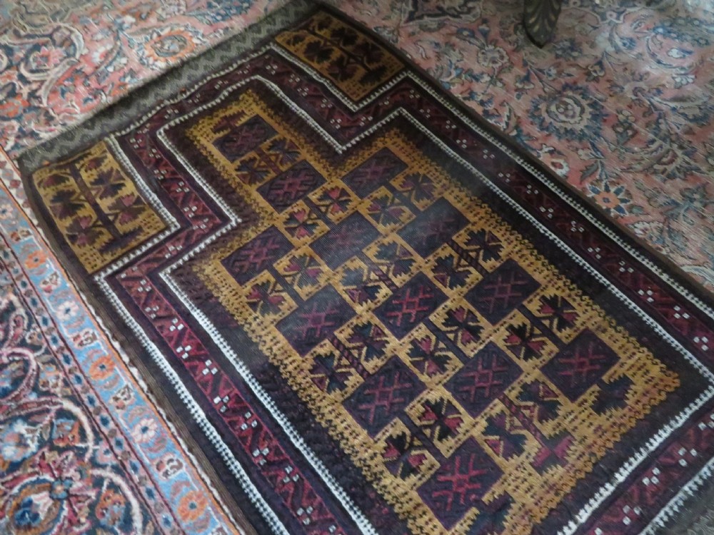An antique Baluch wool prayer rug featuring a stepped arched mihrab design on a camel-coloured field with deep red and navy geometric motifs. View XXI